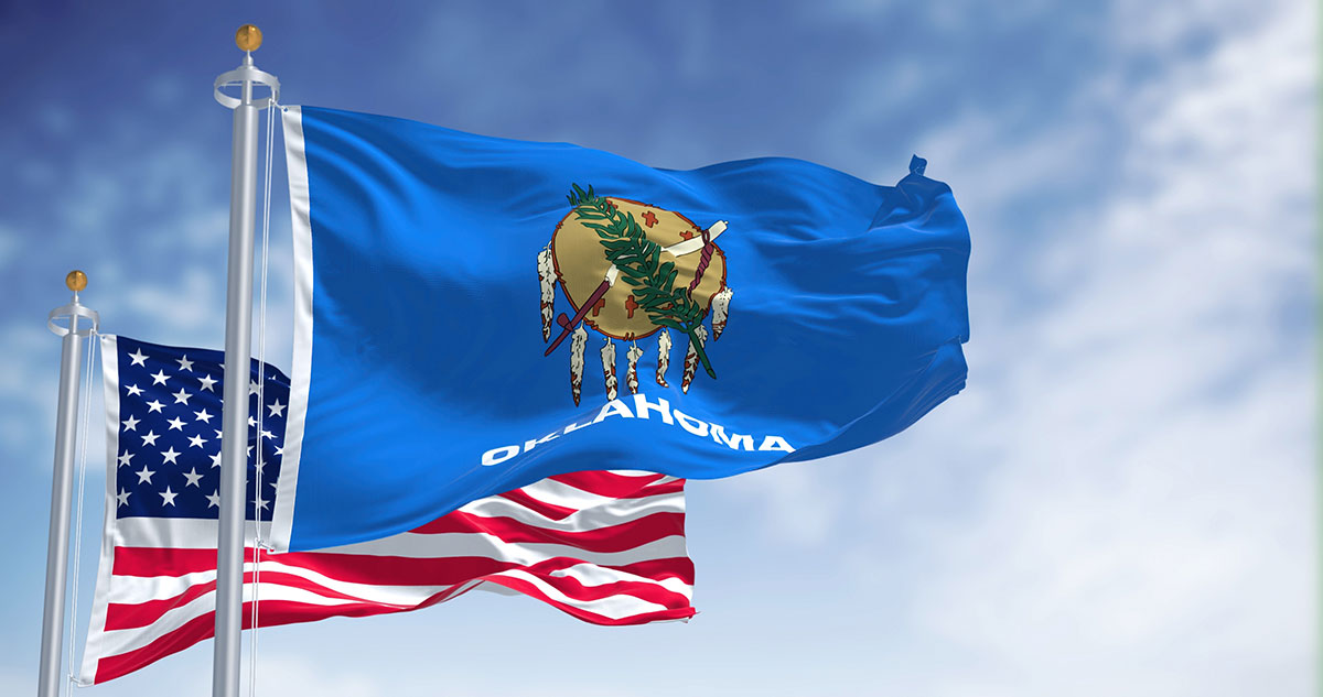 Oklahoma state flag featuring an Osage war shield with six crosses and seven pendant eagle feathers on a medium blue field
